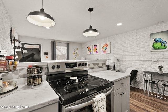 kitchen featuring stainless steel range with electric stovetop, hanging light fixtures, brick wall, and dark wood-style floors