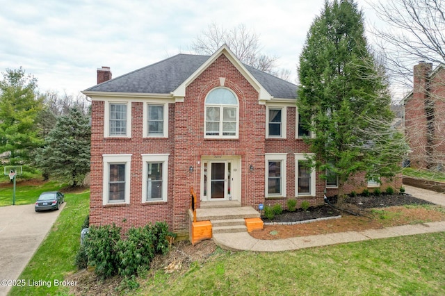 colonial-style house featuring brick siding, a chimney, and a shingled roof