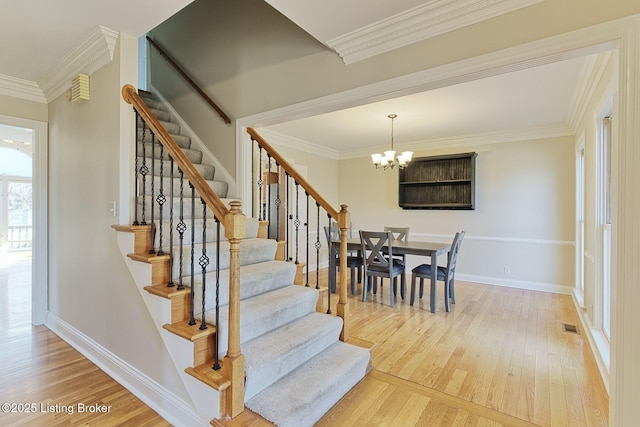 stairway featuring baseboards, visible vents, wood finished floors, crown molding, and a chandelier