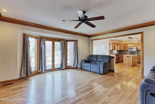 living room featuring light wood finished floors, visible vents, baseboards, ornamental molding, and french doors