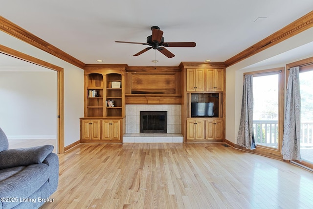 living room with ceiling fan, baseboards, light wood-type flooring, a tiled fireplace, and crown molding