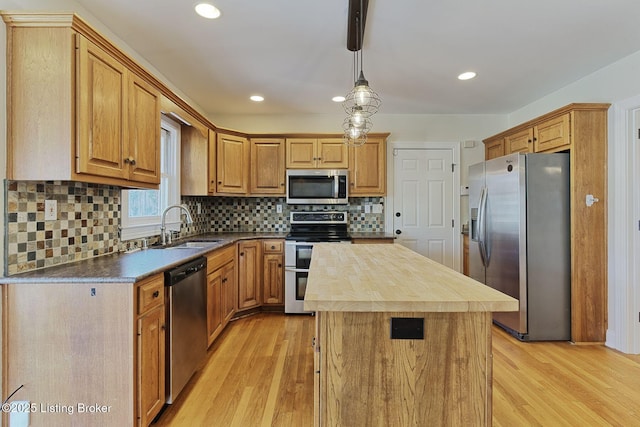 kitchen featuring butcher block counters, light wood-style flooring, appliances with stainless steel finishes, a center island, and a sink