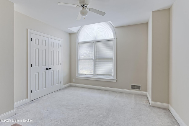 carpeted empty room with baseboards, visible vents, and ceiling fan