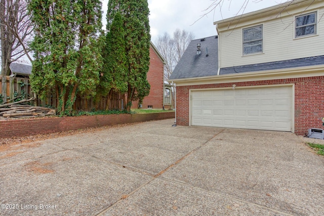 view of side of property with a shingled roof, concrete driveway, brick siding, and fence