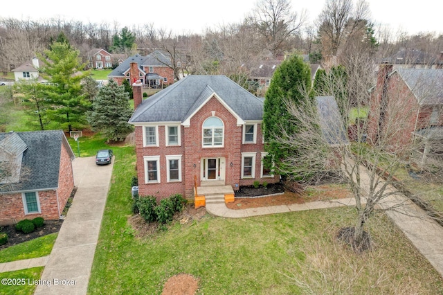 view of front of house featuring a shingled roof, a front yard, a chimney, and brick siding