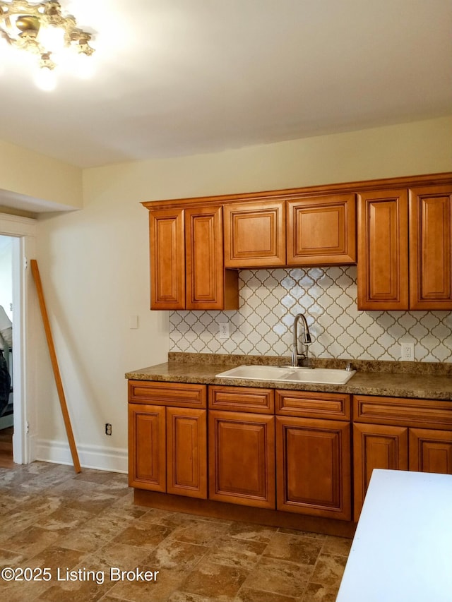 kitchen featuring baseboards, decorative backsplash, brown cabinetry, and a sink