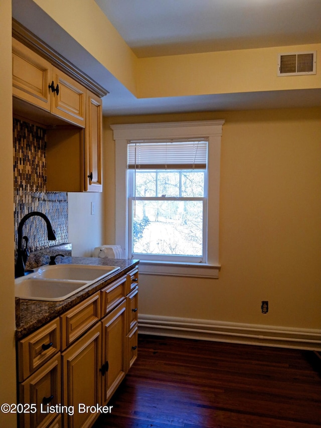 kitchen with dark wood finished floors, dark countertops, visible vents, a sink, and baseboards