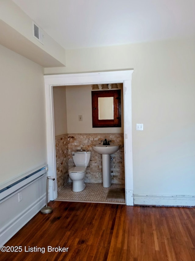 half bathroom with visible vents, toilet, a wainscoted wall, wood finished floors, and a sink