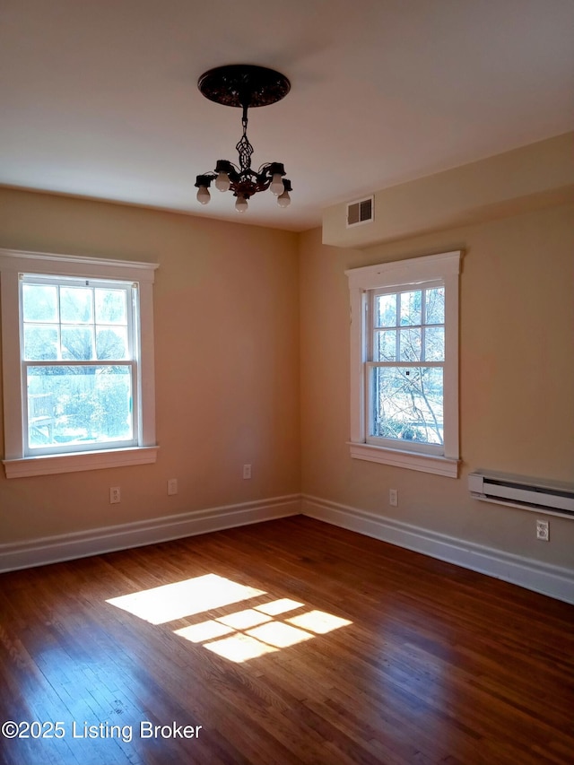 spare room featuring visible vents, an inviting chandelier, a baseboard heating unit, wood finished floors, and baseboards