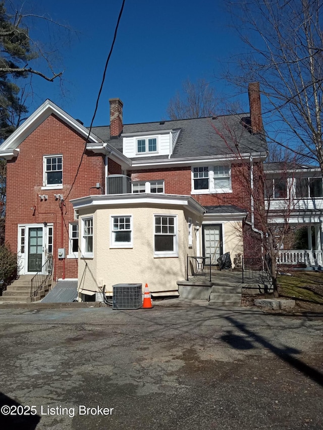 rear view of property featuring entry steps, a chimney, cooling unit, and brick siding