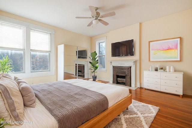 bedroom with wood finished floors, a fireplace with flush hearth, and a ceiling fan