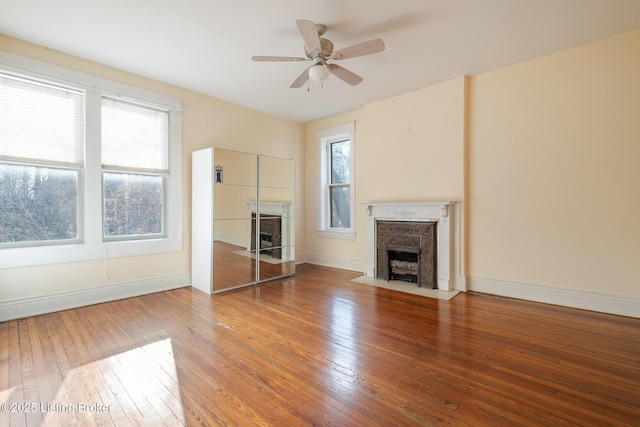 unfurnished living room featuring a ceiling fan, a fireplace with flush hearth, hardwood / wood-style flooring, and baseboards