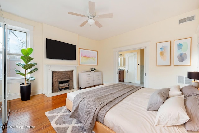 bedroom with wood-type flooring, multiple windows, visible vents, and a fireplace with flush hearth