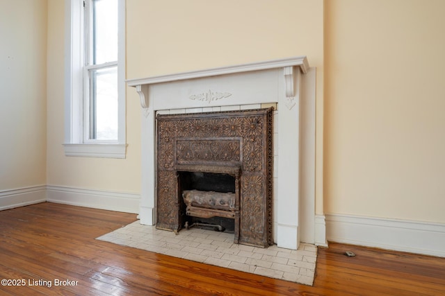 interior details featuring a tile fireplace, baseboards, and wood finished floors