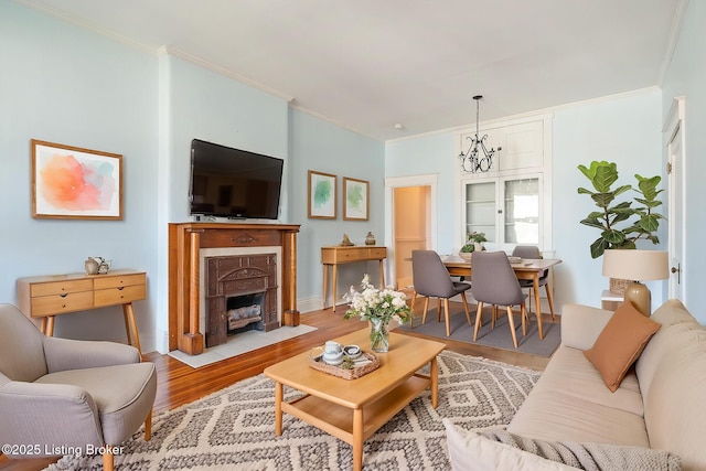 living room with a chandelier, ornamental molding, light wood-type flooring, and a fireplace with flush hearth