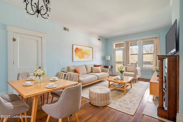 living area featuring a chandelier, visible vents, baseboards, ornamental molding, and hardwood / wood-style floors