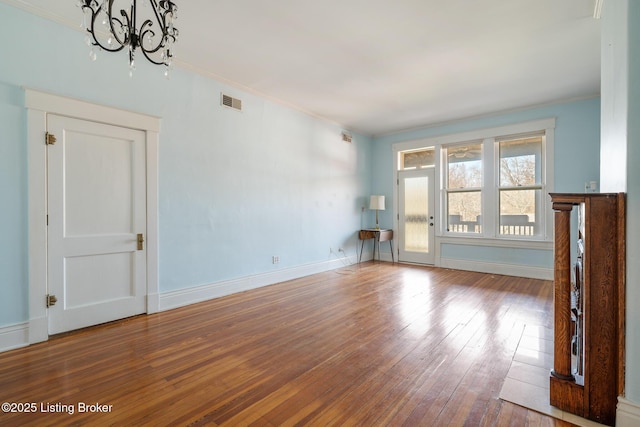 unfurnished living room featuring a notable chandelier, visible vents, baseboards, ornamental molding, and wood-type flooring