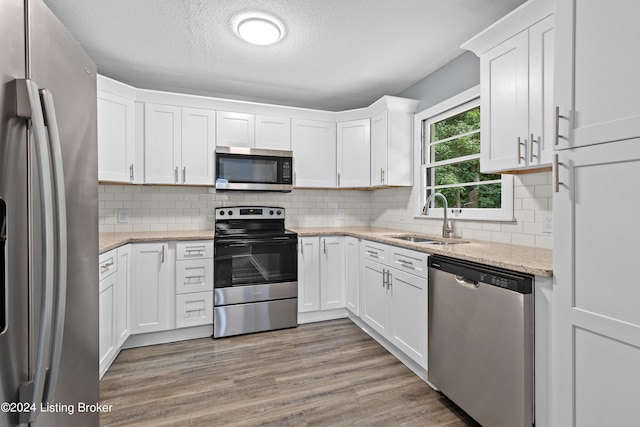 kitchen featuring backsplash, appliances with stainless steel finishes, white cabinets, a sink, and wood finished floors