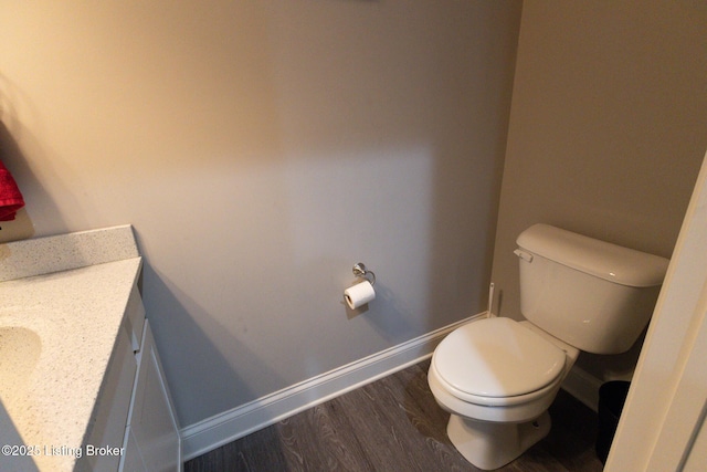 half bath with toilet, baseboards, wood finished floors, and vanity