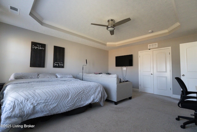 carpeted bedroom featuring a tray ceiling, visible vents, and crown molding