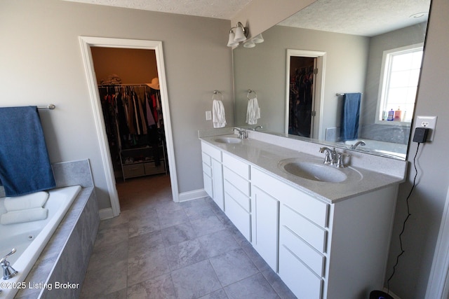 bathroom featuring a textured ceiling, double vanity, a spacious closet, and a sink