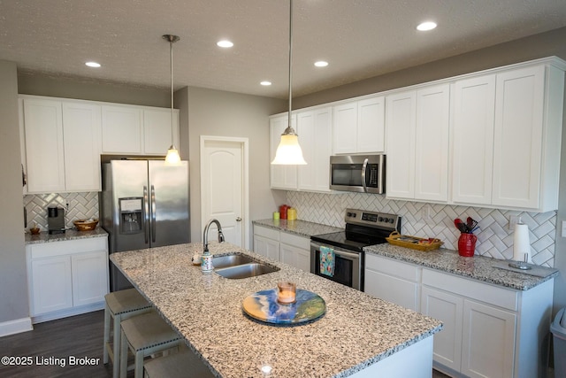 kitchen with dark wood finished floors, stainless steel appliances, white cabinetry, a sink, and a kitchen island with sink