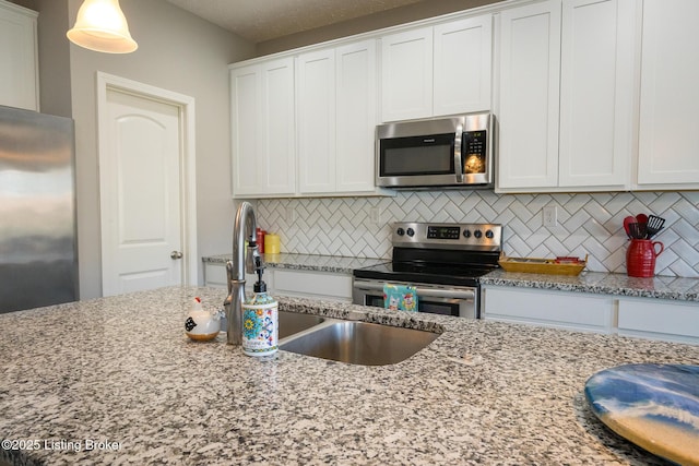 kitchen with light stone counters, a sink, white cabinetry, appliances with stainless steel finishes, and backsplash