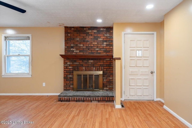 unfurnished living room with a textured ceiling, recessed lighting, wood finished floors, baseboards, and a brick fireplace