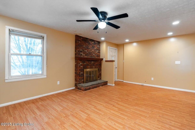 unfurnished living room featuring light wood-type flooring, a fireplace, baseboards, and a textured ceiling