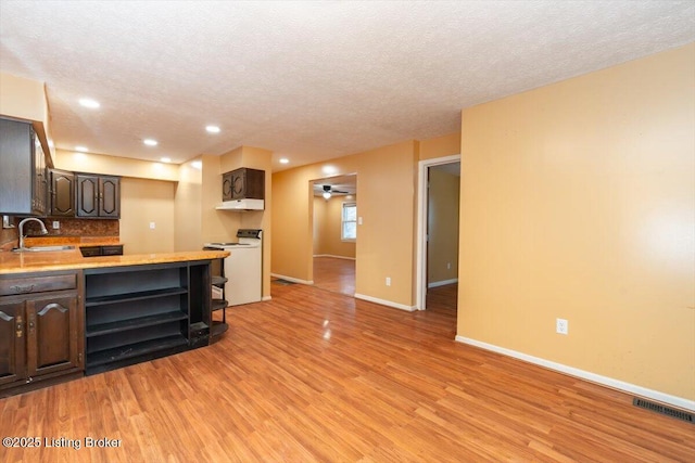 kitchen with dark brown cabinetry, light wood finished floors, visible vents, open shelves, and a sink