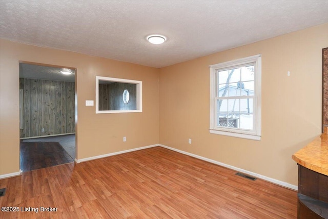 empty room with baseboards, a textured ceiling, visible vents, and wood finished floors