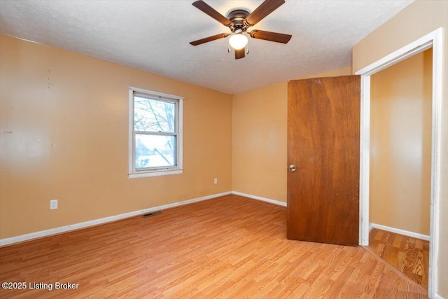 interior space with light wood-style floors, visible vents, a textured ceiling, and baseboards