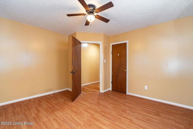 spare room with a textured ceiling, light wood-style flooring, and baseboards