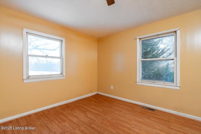 empty room with a textured ceiling, wood finished floors, visible vents, and baseboards