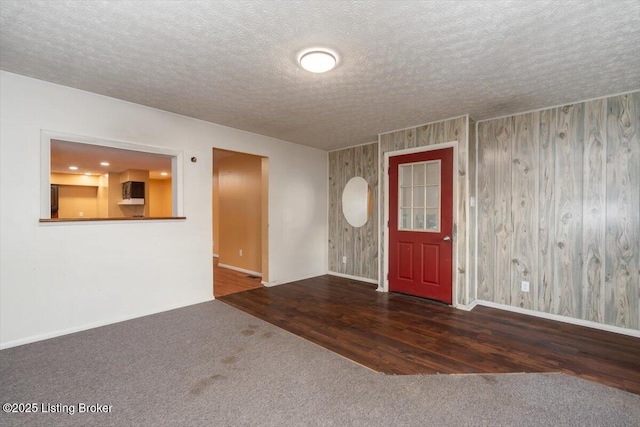 carpeted foyer with a textured ceiling, baseboards, and wood finished floors