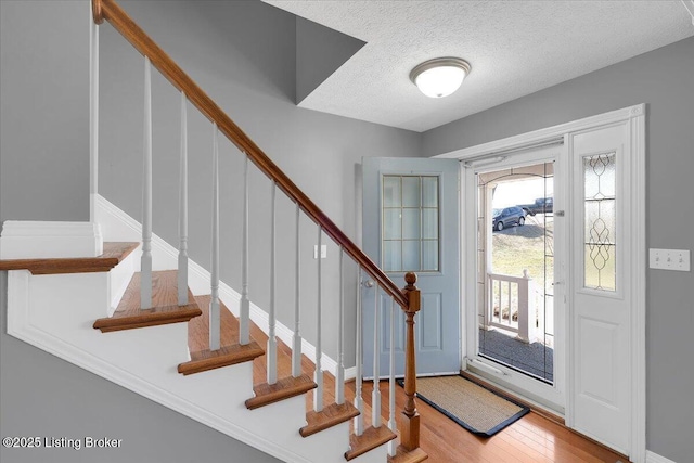 foyer entrance featuring a textured ceiling, stairway, and wood finished floors