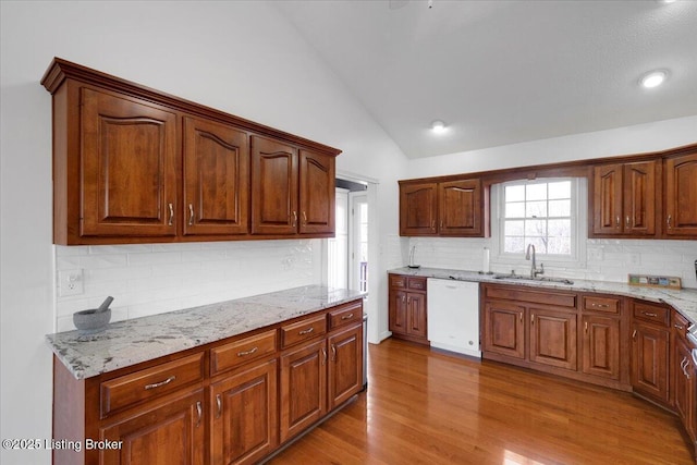 kitchen featuring lofted ceiling, wood finished floors, a sink, light stone countertops, and dishwasher