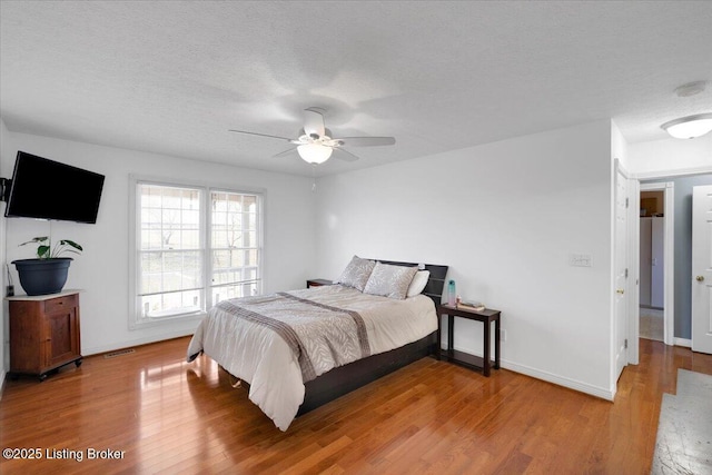 bedroom with light wood-style floors, visible vents, a textured ceiling, and baseboards