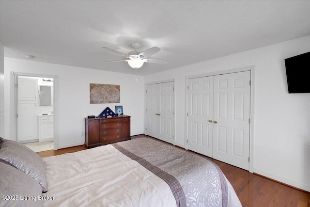 bedroom featuring baseboards, connected bathroom, a ceiling fan, wood finished floors, and two closets