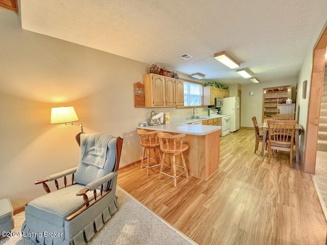 kitchen with light countertops, visible vents, light wood-style floors, white appliances, and a peninsula