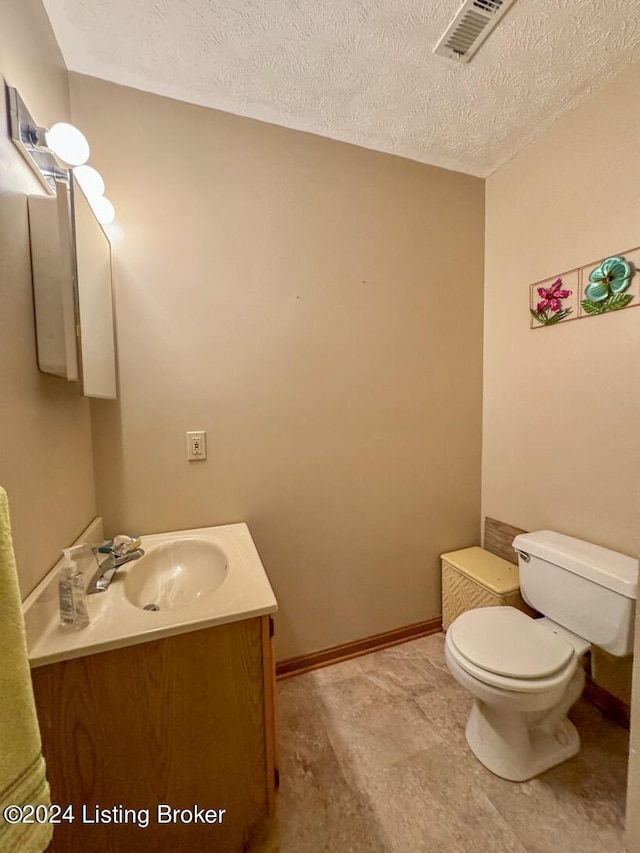 bathroom featuring visible vents, toilet, vanity, a textured ceiling, and baseboards