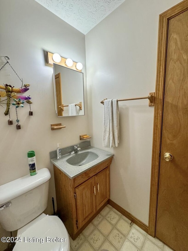 half bath featuring a textured ceiling, toilet, vanity, baseboards, and tile patterned floors