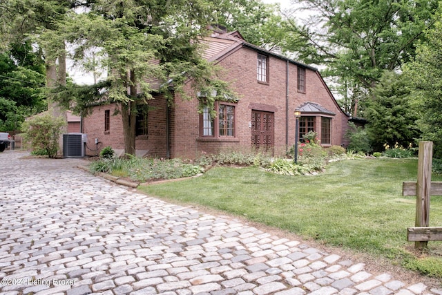 exterior space featuring brick siding, cooling unit, and a front lawn