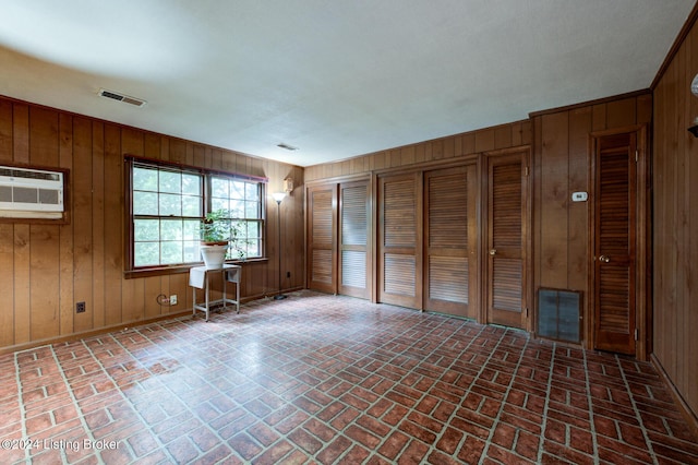 spare room featuring brick floor, visible vents, wooden walls, and a wall unit AC