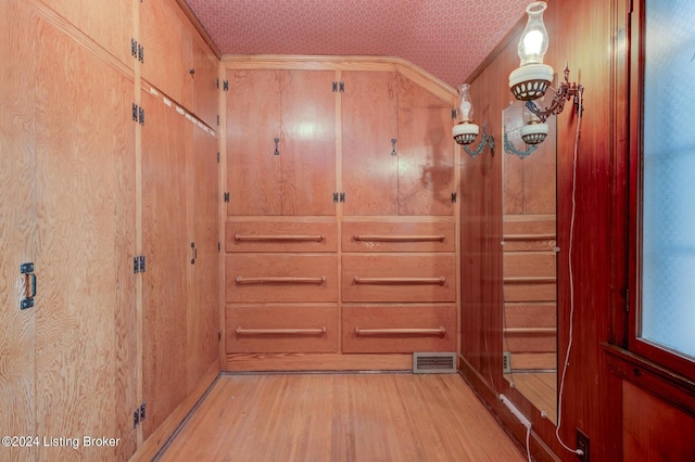 entryway featuring visible vents, wooden walls, light wood-style flooring, and vaulted ceiling