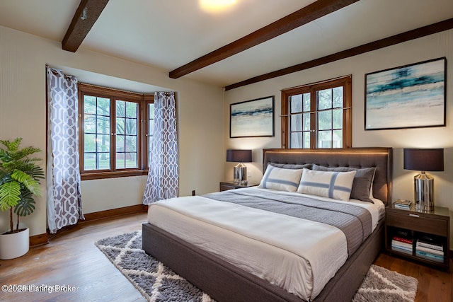 bedroom with baseboards, beam ceiling, and wood finished floors