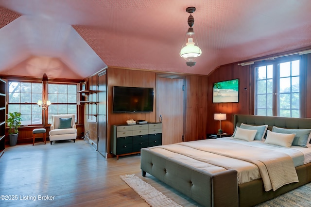 bedroom featuring light wood finished floors, wooden walls, multiple windows, and vaulted ceiling