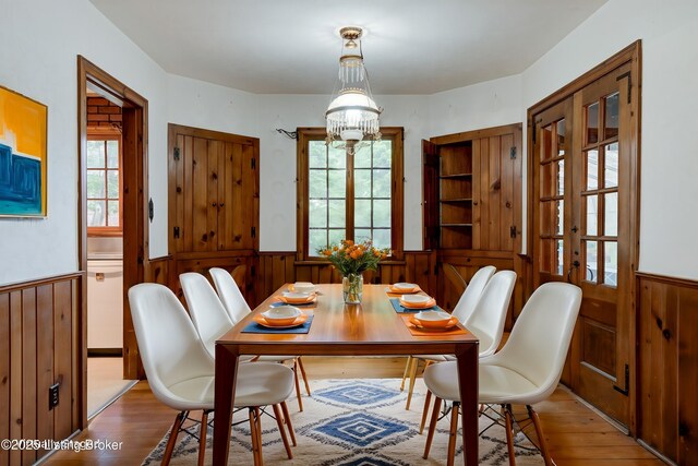 dining area with wood finished floors, wooden walls, a chandelier, and wainscoting