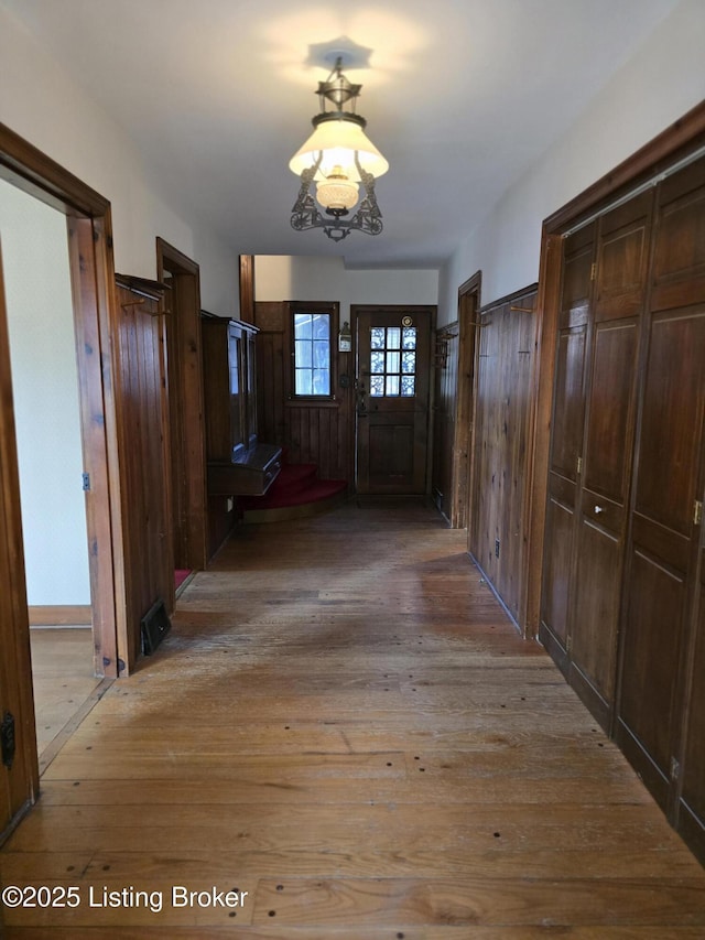 hall featuring light wood-type flooring, wooden walls, and a notable chandelier