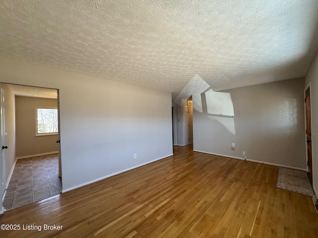 unfurnished room with a textured ceiling, wood finished floors, and baseboards